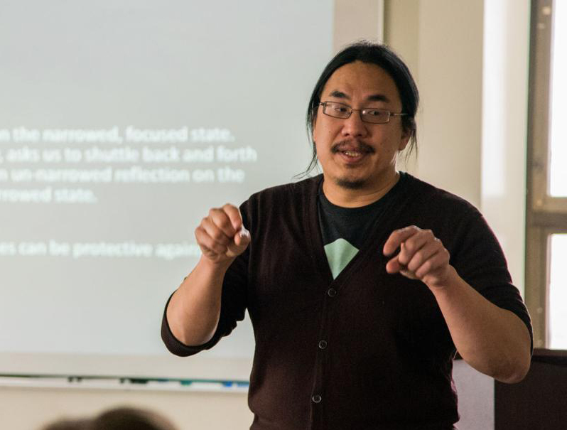 Photograph of philosopher C. Thi Nguyen teaching in front of a projector screen.
